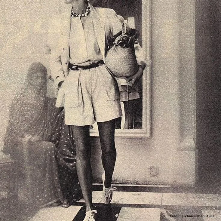 Sepia archival fashion photograph — a figure in pleated shorts, blazer, and woven shoulder bag — evoking the 1980s Indian retro elegance that informs the Sentiments aesthetic. Credit: archaicarmani, 1983.