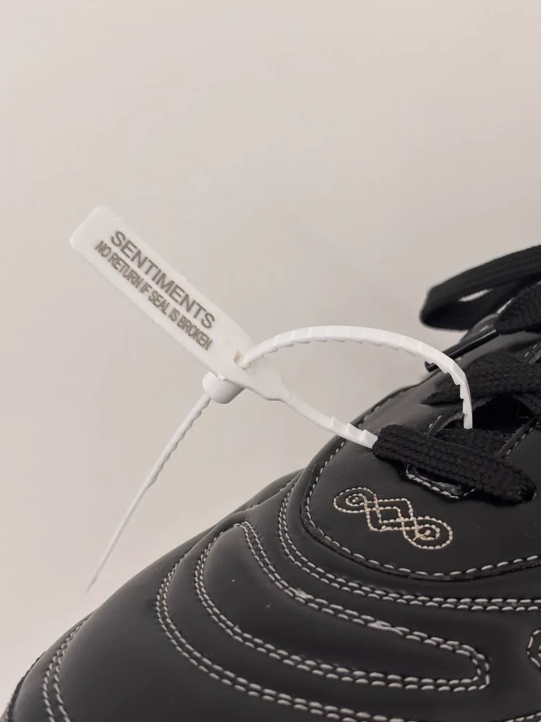 A close-up of the same Sentiments tamper-evident seal tag from a different angle — the SENTIMENTS · NO RETURN IF SEAL IS BROKEN text visible on the dangling lace-threaded tag.